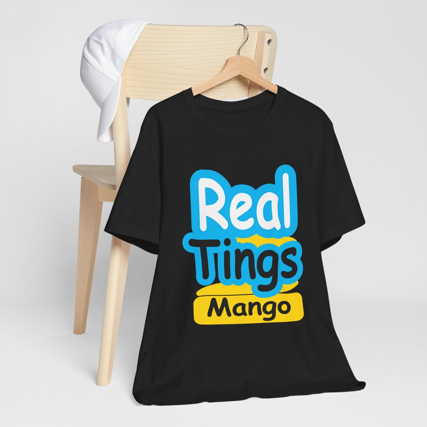 Black t-shirt with 'Real Tings Mango' text on a wooden chair against a white background